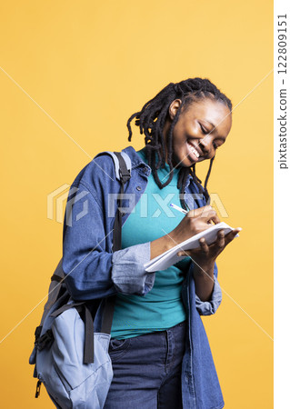 Happy professional brainstorming ideas, writing on document using pen. Upbeat african american photographer using clipboard to complete shoot list for upcoming photography work, studio background 122809151