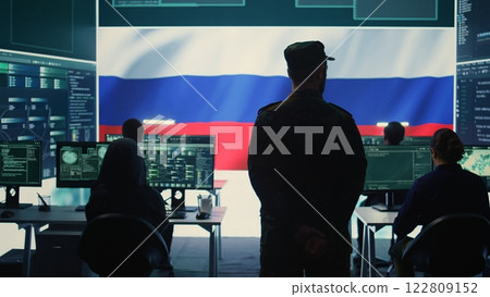 Military hacker from Russian army working in governmental control room cracking rival states network systems to spread fake news and hybrid war propaganda. Brainwashing ideology strategy. Camera B. 122809152