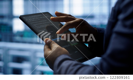Software developer does yearly checkup using tablet to prolong data center electronics life span. Close up shot of worker in server room monitoring server infrastructure using digital device, camera A 122809161