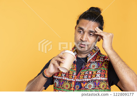 Tired man feeling pain, suffering from headache after sleepless night, drinking coffee. Injured person rubbing head temples, feeling discomforting strain, sipping caffeine drink, studio background 122809177