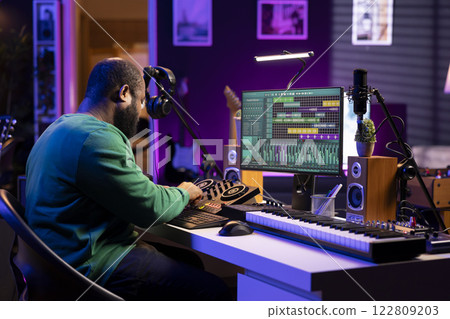 Skilled male composer producing new songs on his mixing console, operating on professional gear in home studio. Artist audio engineer twisting knobs to adjust sound levels on tracks. 122809203