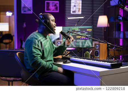 Artist composer recording a new track on his home studio microphone, editing his song with professional gear. Adjusting volume levels and adding sound effects, mix and master. 122809218