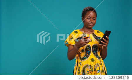 Cheerful woman customer doing online shopping and ordering products with her card, paying via electronic banking service. Young person feeling happy and excited buying on sale. Camera B. 122809246
