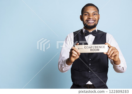 Hospitality industry staff showing the wall sign pointer to the conference room, offering directions for guests at five star hotel. Bellboy porter holds the indicator to the amenities. Hospitality industry staff showing the wall sign pointer to the conference room, offering directions for guests at five star hotel. Bellboy porter holds the indicator to the amenities. 122809283