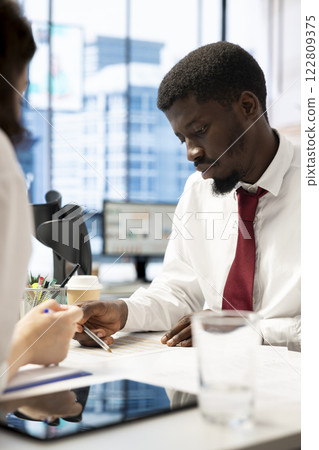 HR worker negotiating job offers and salary packages with african american candidate after successful interview. Manager in workplace analyzing man resume, cover letter and background information 122809375