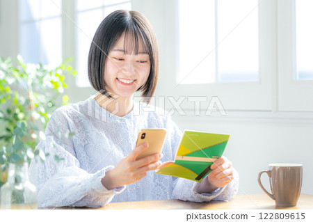 A woman looking at her bankbook and smartphone 122809615