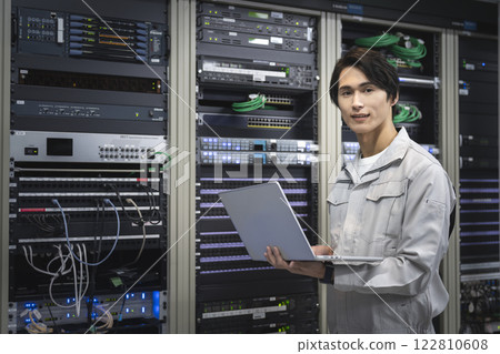 伺服器工程師圖片：一位穿著工作服的年輕工程師拿著電腦看著相機 122810608