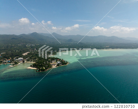 Scenic coastline featuring turquoise waters and a mountain backdrop with clear skies. Ko Pha Ngan, Thailand. 122810710