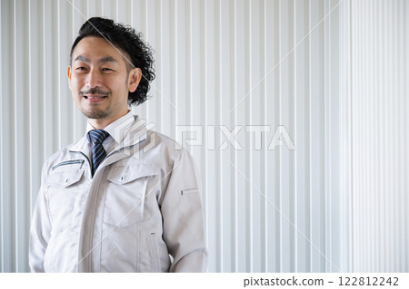 Bearded man wearing work clothes looking at camera in front of a factory Bearded man wearing work clothes looking at camera in front of a factory 122812242
