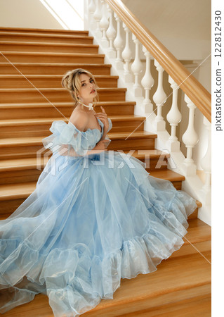 Young woman in light blue evening dress climbs large wooden staircase in luxurious manor Young woman in light blue evening dress climbs large wooden staircase in luxurious manor 122812430