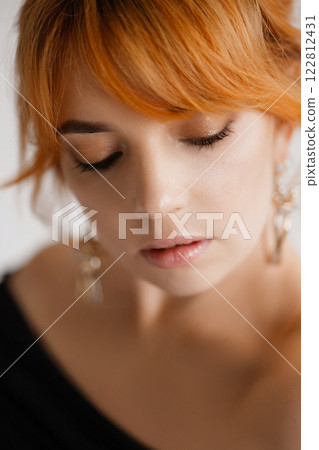 Close-up portrait of a young woman with bright red hair. Eyes closed. 122812431