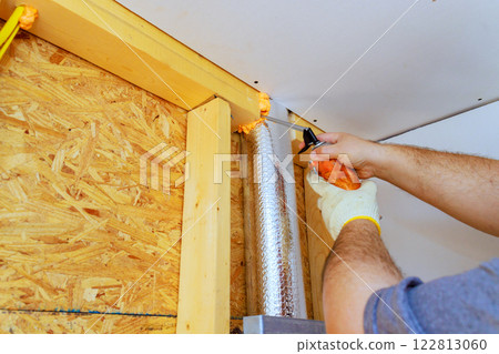 Worker is applying foam insulation to vent pipe in residential area, on energy efficiency during renovations. 122813060
