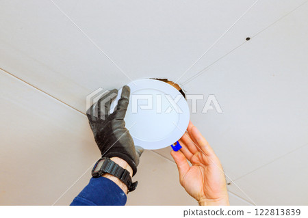 An electrician is carefully placing recessed light fixture into ceiling opening, during home renovation skills. 122813839