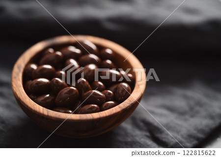 Milk chocolate dragee in olive wood bowl on linen background 122815622