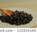Coffee beans on a white plate with a brown wooden spoon. 122816160