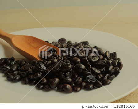 Coffee beans on a white plate with a brown wooden spoon. 122816160