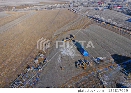 Aerial view of rural landscape showing farm fields, icy terrain, and distant village during winter morning 122817639