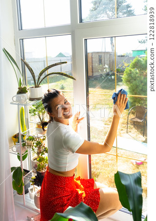 Woman manually washes the window of house with rag cleaner and mop inside the interior with home plants on windowsill. Restoring order and cleanliness in the spring, cleaning servise Woman manually washes the window of house with rag cleaner and mop inside the interior with home plants on windowsill. Restoring order and cleanliness in the spring, cleaning servise 122818939