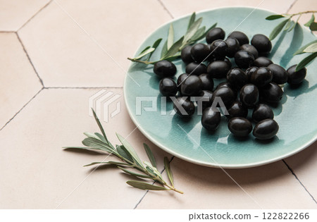 Black olives served on ceramic plate with olive branches on tiled surface 122822266