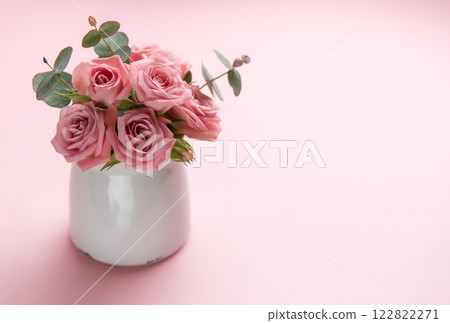 Pink roses and eucalyptus leaves decorating a white vase on a pink background Pink roses and eucalyptus leaves decorating a white vase on a pink background 122822271