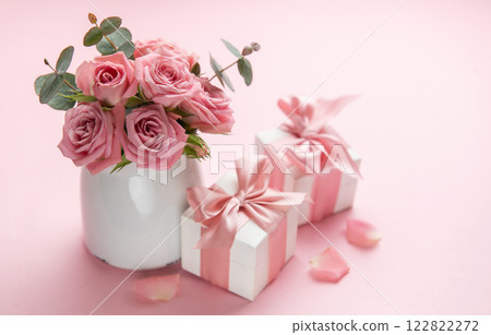 Pink roses in white vase decorating gift boxes with pink ribbons on pink background 122822272