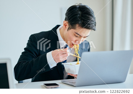 一名 20 多歲的年輕男子邊工作邊吃泡麵 一名 20 多歲的年輕男子邊工作邊吃泡麵 122822692