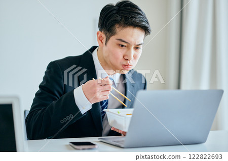 一名 20 多歲的年輕男子邊工作邊吃泡麵 一名 20 多歲的年輕男子邊工作邊吃泡麵 122822693