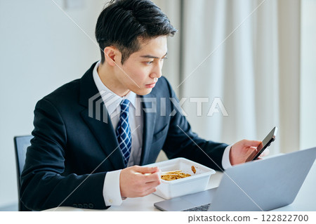 A young man in his twenties eating cup noodles while operating a smartphone A young man in his twenties eating cup noodles while operating a smartphone 122822700