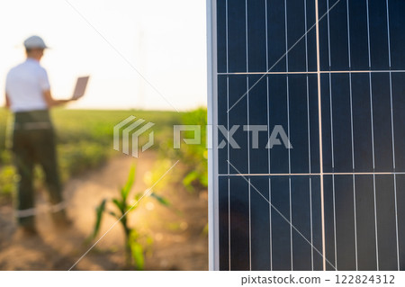 Woman farmer wearing white cap and t-shirt with laptop next to solar panel. 122824312