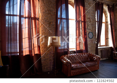 Windows at empty Library room with a brick wall. Leather sofa in a vintage style. The furniture in the room. Dark brown interior 122824502