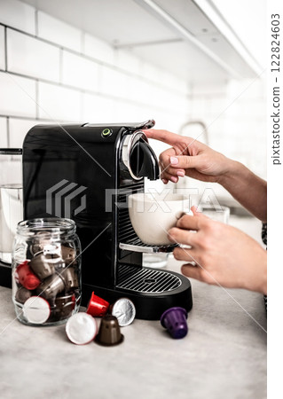 Girl with capsule coffee machine and cup at kitchen. Woman preparing italian caffeine beverage using professional espresso maker Girl with capsule coffee machine and cup at kitchen. Woman preparing italian caffeine beverage using professional espresso maker 122824603
