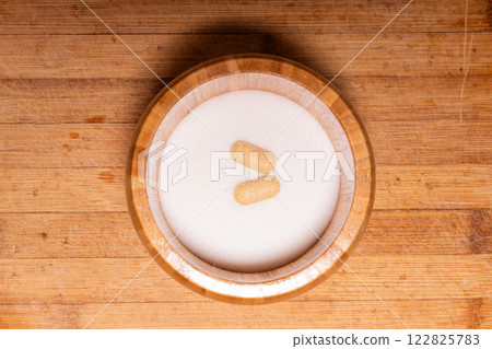Two yellowish tablets on white salt powder in a wooden bowl, representing a blend of kitchen ingredients and medication. Two yellowish tablets on white salt powder in a wooden bowl, representing a blend of kitchen ingredients and medication. 122825783