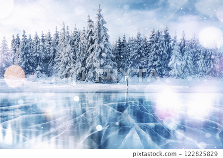 Blue ice and cracks on the surface of the ice. Frozen lake in winter mountains. It is snowing. The hills of pines. Winter. Carpathian Ukraine Europe 122825829