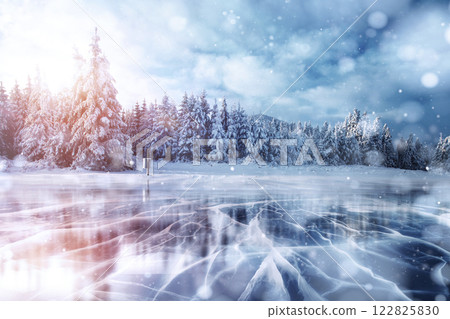 Blue ice and cracks on the surface of the ice. Frozen lake in winter mountains. It is snowing. The hills of pines. Winter. Carpathian Ukraine Europe 122825830
