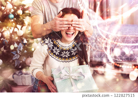 Young couple celebrating Christmas. A man suddenly presented a present to his wife. The concept of family happiness and well-being. Bokeh light soft effect 122827515