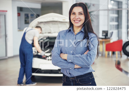Woman at a car garage getting mechanical service. The mechanic works under the hood of the car 122828475