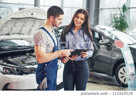 A man mechanic and woman customer discussing repairs done to her vehicle A man mechanic and woman customer discussing repairs done to her vehicle 122828529