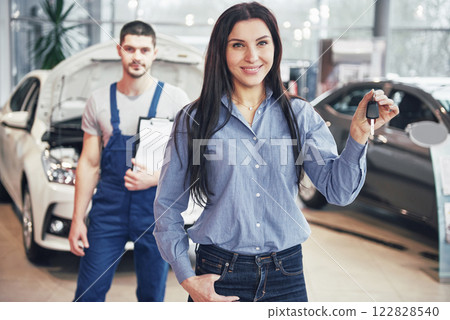 A young woman takes a car from the car service center. She is happy because the work is done perfectly A young woman takes a car from the car service center. She is happy because the work is done perfectly 122828540