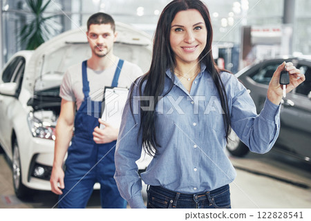 A young woman takes a car from the car service center. She is happy because the work is done perfectly 122828541