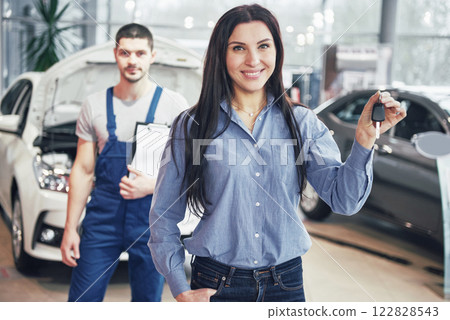 A young woman takes a car from the car service center. She is happy because the work is done perfectly 122828543