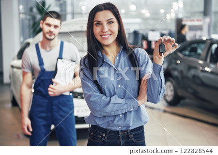 A young woman takes a car from the car service center. She is happy because the work is done perfectly A young woman takes a car from the car service center. She is happy because the work is done perfectly 122828544