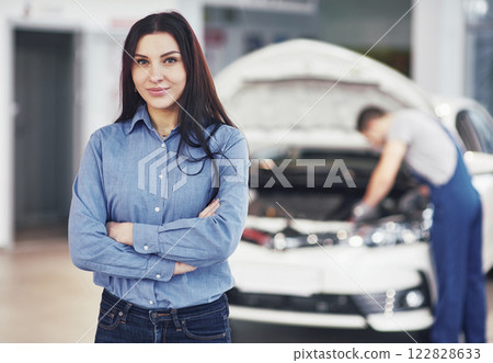 Woman at a car garage getting mechanical service. The mechanic works under the hood of the car 122828633