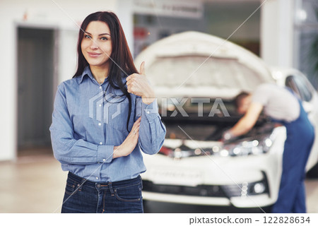 The woman approves the work done by the client. The mechanic works under the hood of the car The woman approves the work done by the client. The mechanic works under the hood of the car 122828634