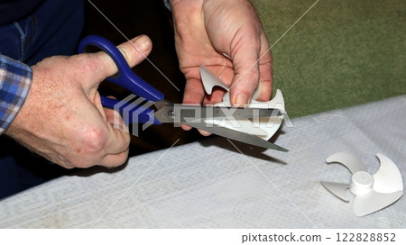 Repairing a refrigerator fan blade with scissors to restore proper cooling functionality at home 122828852