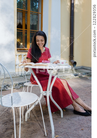 young African American woman in burgundy dress looks at menu and orders tea in coffee shop in park young African American woman in burgundy dress looks at menu and orders tea in coffee shop in park 122829356