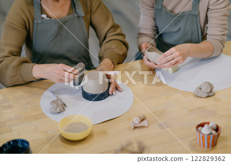 Two women work together with clay, developing skills and enjoying the artistic process. Mother and daughter engage in an art workshop, strengthening their bond through handcraft Two women work together with clay, developing skills and enjoying the artistic process. Mother and daughter engage in an art workshop, strengthening their bond through handcraft 122829362