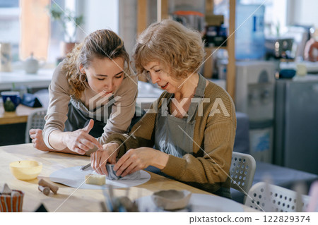 Mother and daughter engage in an art workshop, strengthening their bond through handcraft. Two generations of women take part in a pottery lesson, sharing knowledge and creativity. 122829374
