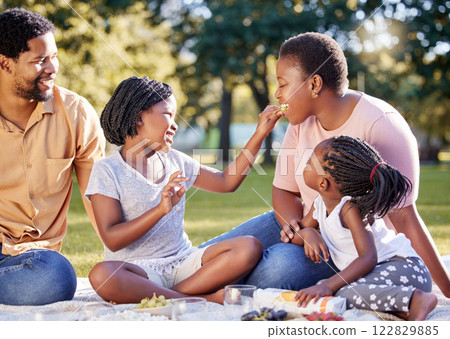 Picnic, summer and happy with black family in park, eating fruit together for care, bonding or holiday. Vacation, happy family and health with parents and children sitting in countryside environment 122829885