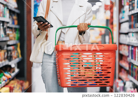 Grocery shopping, retail and black woman with phone in store, shop or supermarket. Girl buying groceries or purchasing products at a food mart or outlet while texting on mobile or smartphone. 122830426