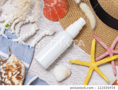 Sunscreen cream bottle on hat near towel, seashells and starfishes top view, cosmetic mockup 122830459